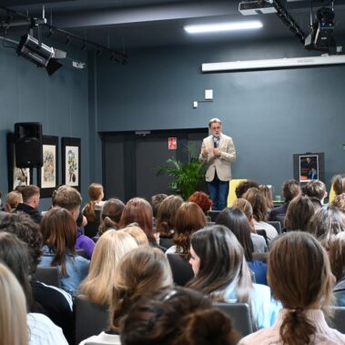 Widok na salę młodzież i na scenie stoi Michał Rusinek
