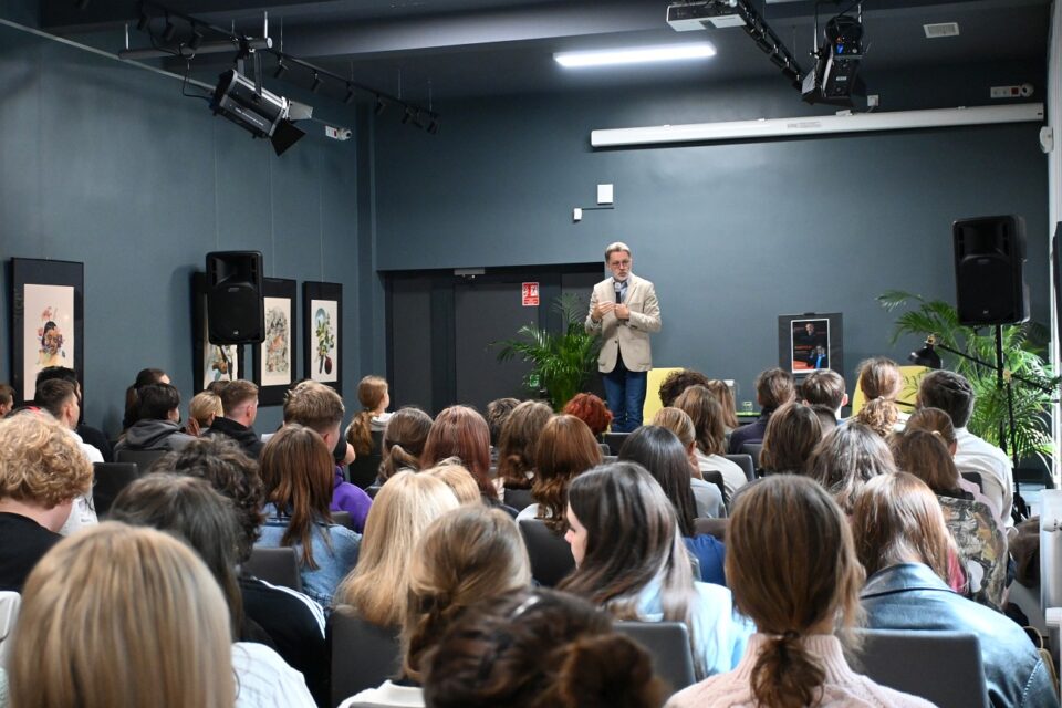 Widok na salę młodzież i na scenie stoi Michał Rusinek