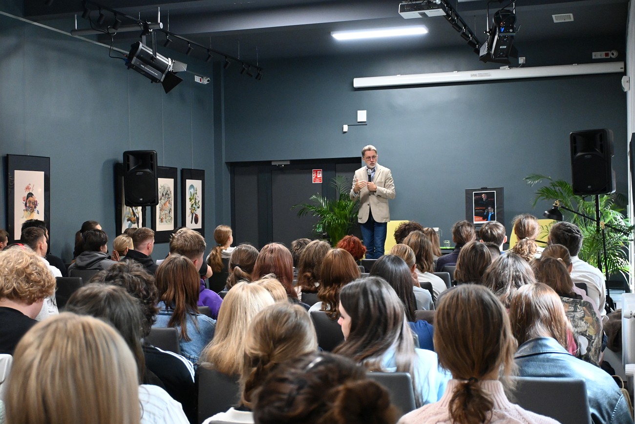 Widok na salę młodzież i na scenie stoi Michał Rusinek