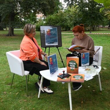 Czytelniczka czyta na głos książkę w towarzystwie bibliotekarki