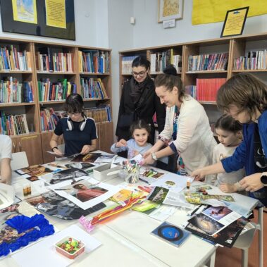 Dzieci w towarzystwie bibliotekarki i matek wykonują prace plastyczne, na stole leżą różne materiały