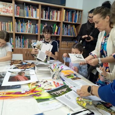 Dzieci w towarzystwie bibliotekarki i matek wykonują prace plastyczne, na stole leżą różne materiały