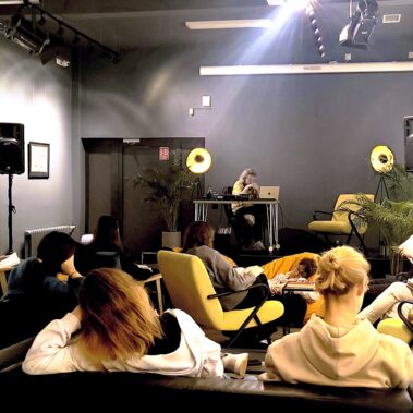 Reading Party w Bibliotece czyli Muzyka dla Książek — widok na salę, uczestnicy czytają, na scenie DJ Kacper Kapsa odtwarza muzykę