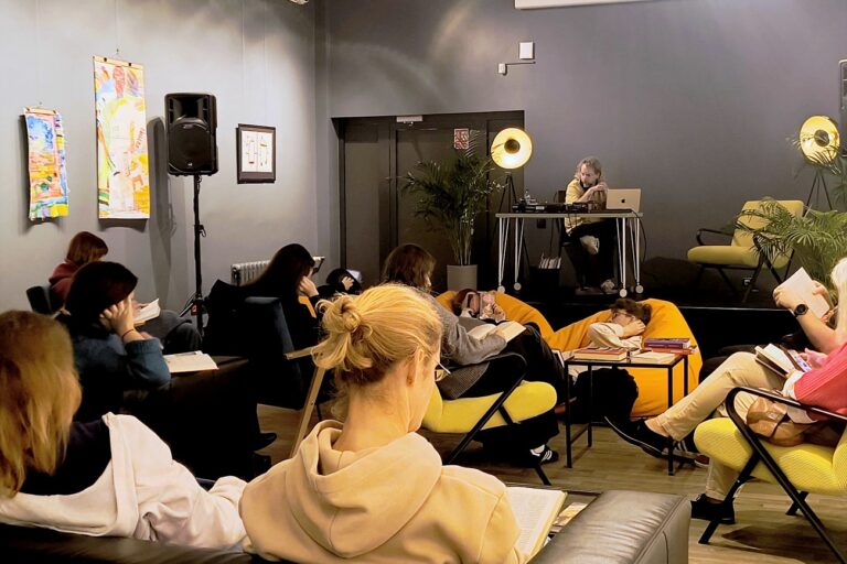 Reading Party w Bibliotece czyli Muzyka dla Książek — widok na salę, uczestnicy czytają, na scenie DJ Kacper Kapsa odtwarza muzykę