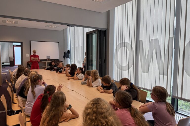 Bibliotekarka czyta na głos książkę, dzieci słuchają