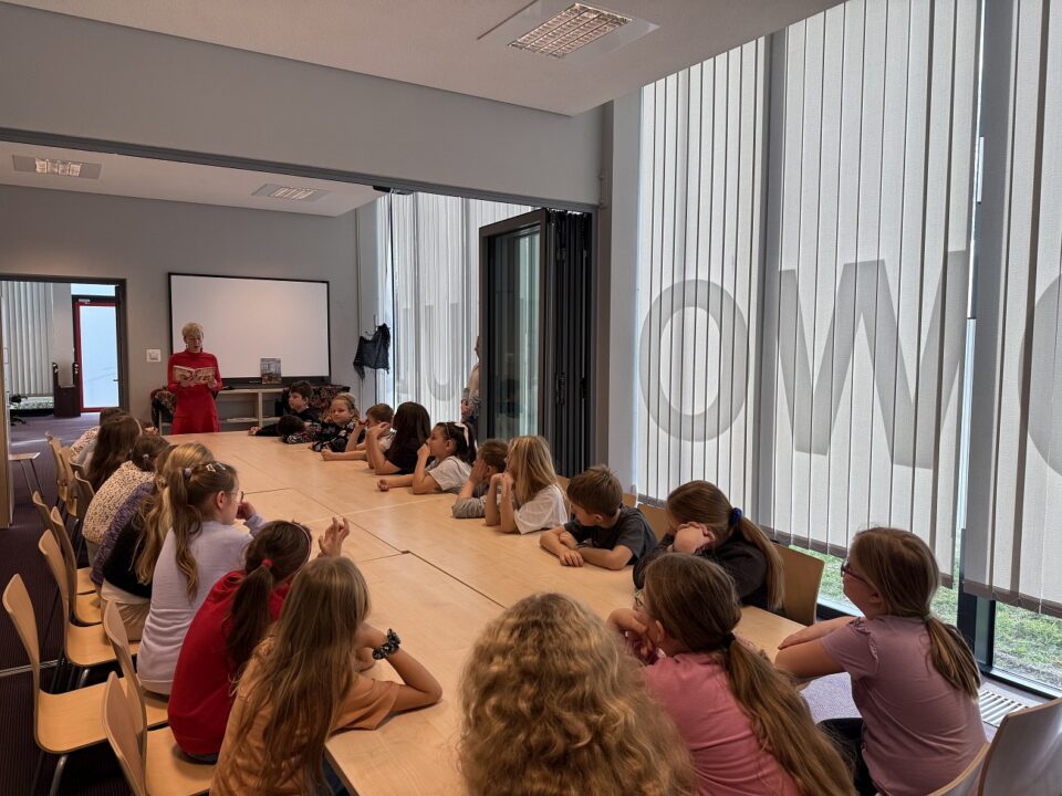 Bibliotekarka czyta na głos książkę, dzieci słuchają