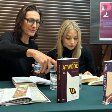 Klaudia Cygoń-Majchrowska i Aleksandra Maj siedzą przy stole, jedna z nich czyta na głos