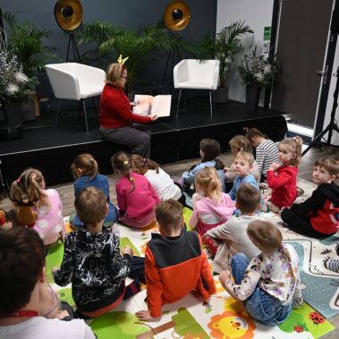 Druga bibliotekarka czyta książkę na głos, dzieci słuchają, inne ujęcie.