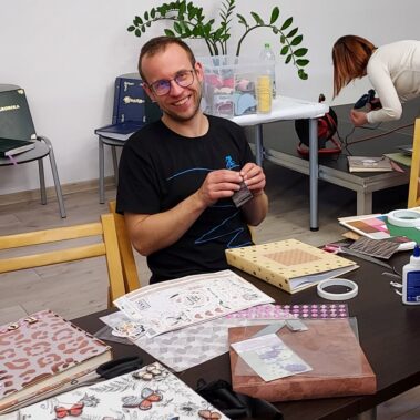 Pan uśmiecha przy pracy, a stole leżą różne materiały
