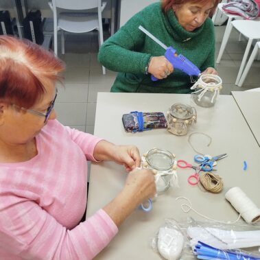 Panie przy pracy nad słoikami, a stole leżą różne materiały.