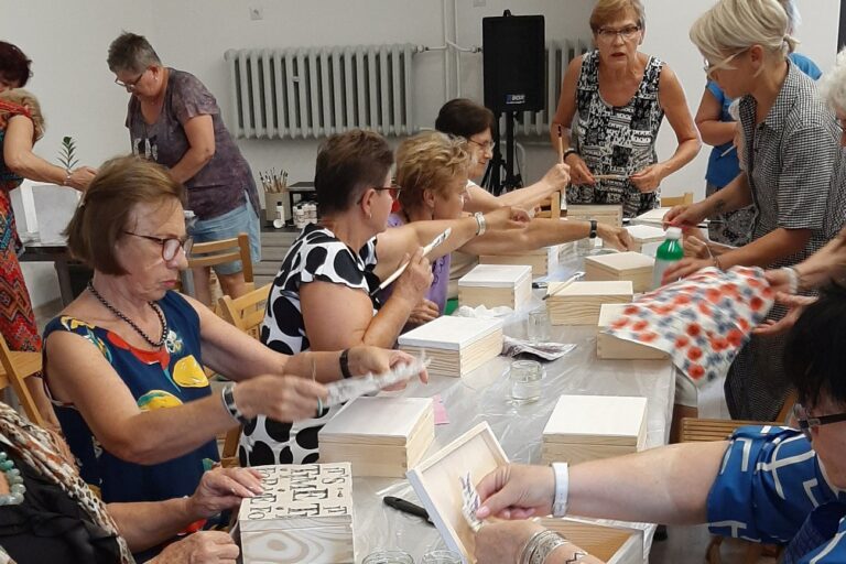Panie przy pracy plastycznej, na stole leżą różne materiały i pudełka