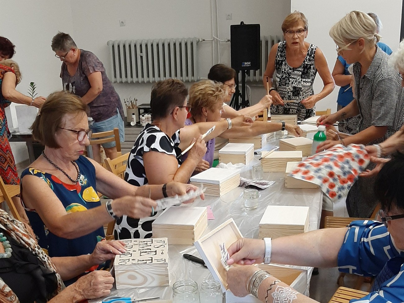 Panie przy pracy plastycznej, na stole leżą różne materiały i pudełka