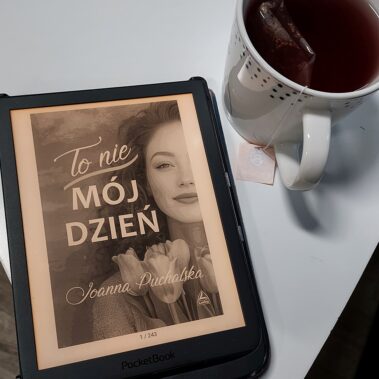 Na stoliku leży czytnik ebooka z „To nie mój dzień”, obok kubek z herbatą