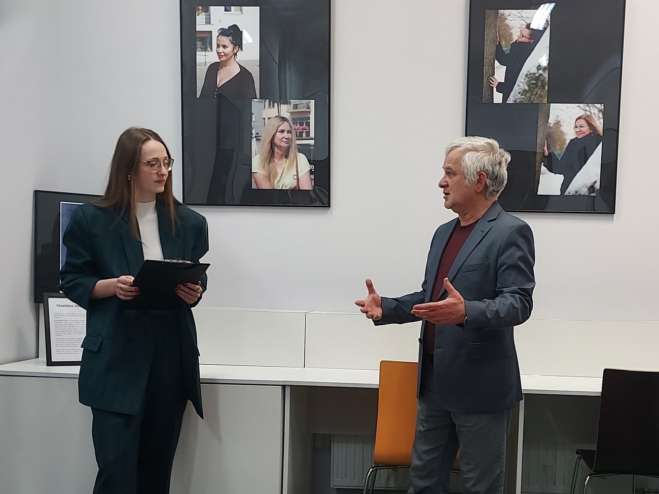 Prowadząca spotkanie rozmawia z Stanisławem Junkiertem, w tle wiszą zdjęcia z wystawy
