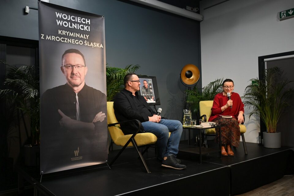 Na scenie siedzą Wojciech Wolnicki i prowadząca spotkanie