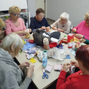 Seniorki przy pracy plastycznej, na stole leżą różne materiały, inne ujęcie