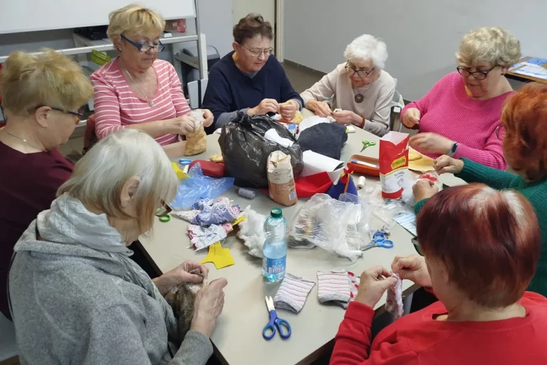 Seniorki przy pracy plastycznej, na stole leżą różne materiały, inne ujęcie