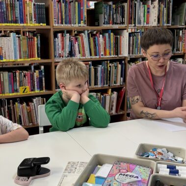 Bibliotekarka czyta na głos książkę, dzieci słuchają