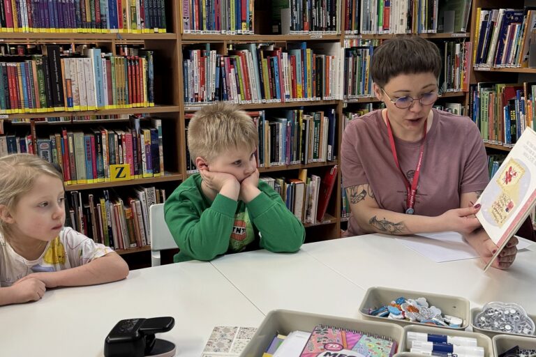 Bibliotekarka czyta na głos książkę, dzieci słuchają