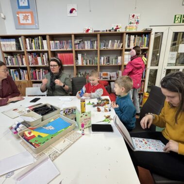 Dzieci i rodzice przy pracy plastycznej i jednocześnie trwa rozmowa z bibliotekarką