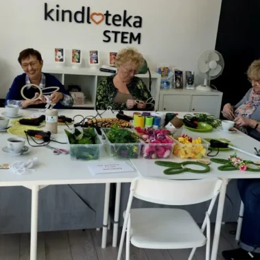 Seniorki siedzą przy stole i wykonują prace plastyczne