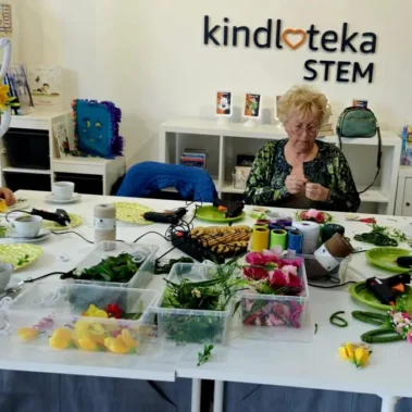 Seniorki przy pracy plastycznej, na stole leżą różne materiały, inne ujęcie