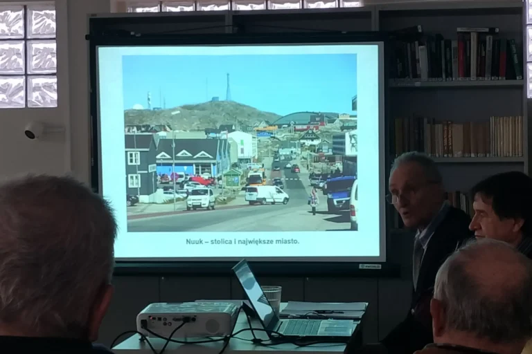 Na ekranie jest wyświetlany slajd — zdjęcie stolicy Grenlandii — Nuuk, wygląda skromnie bez wieżowców.