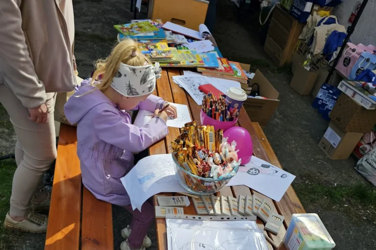 Dziewczynka rysuje, a stole leżą różne rysunki i przybory do rysowania oraz słodycze