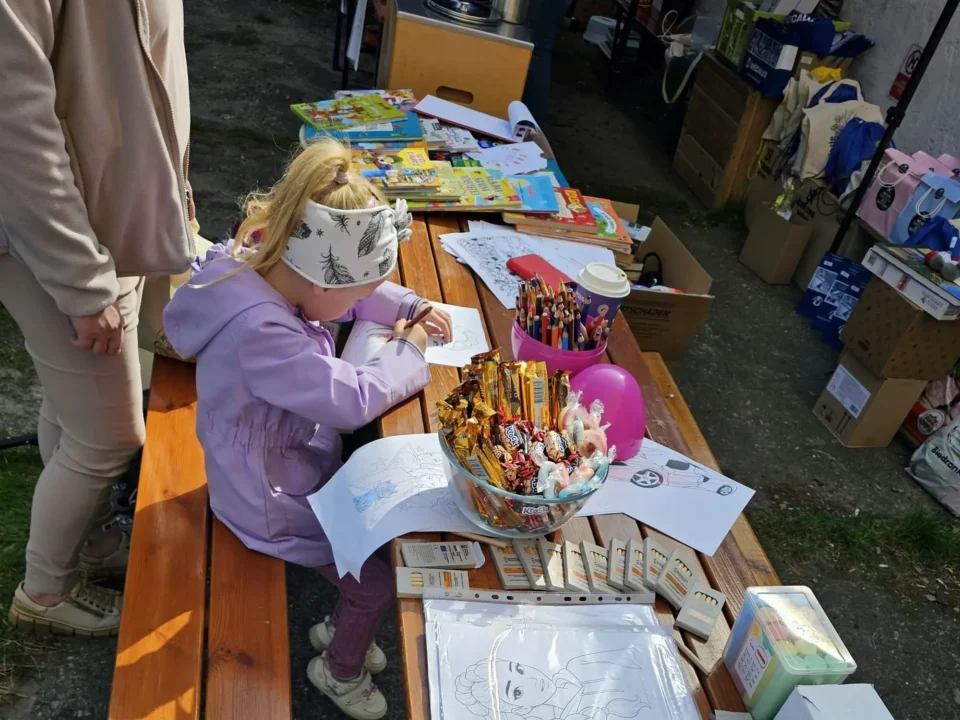 Dziewczynka rysuje, a stole leżą różne rysunki i przybory do rysowania oraz słodycze